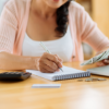 Woman at desk holding money and making a list